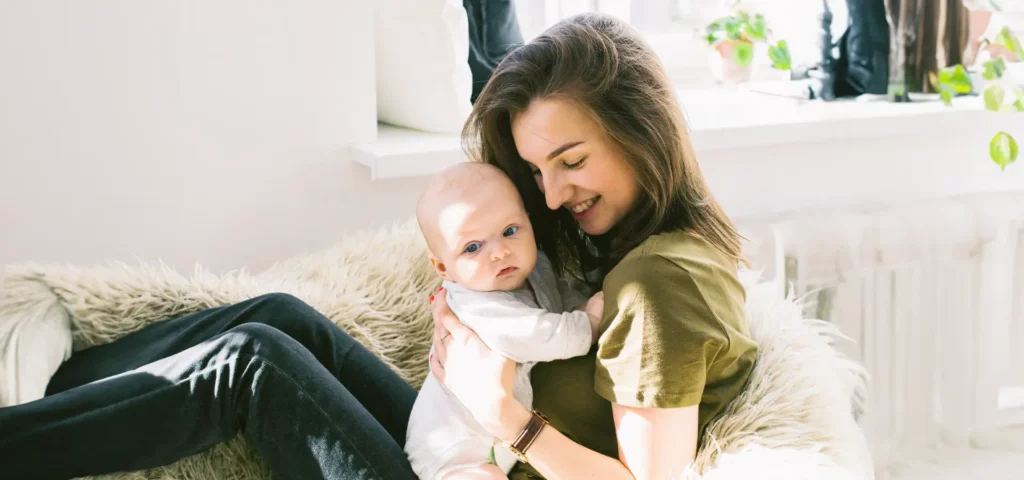 Frau hält Baby liebevoll im Wohnzimmer.