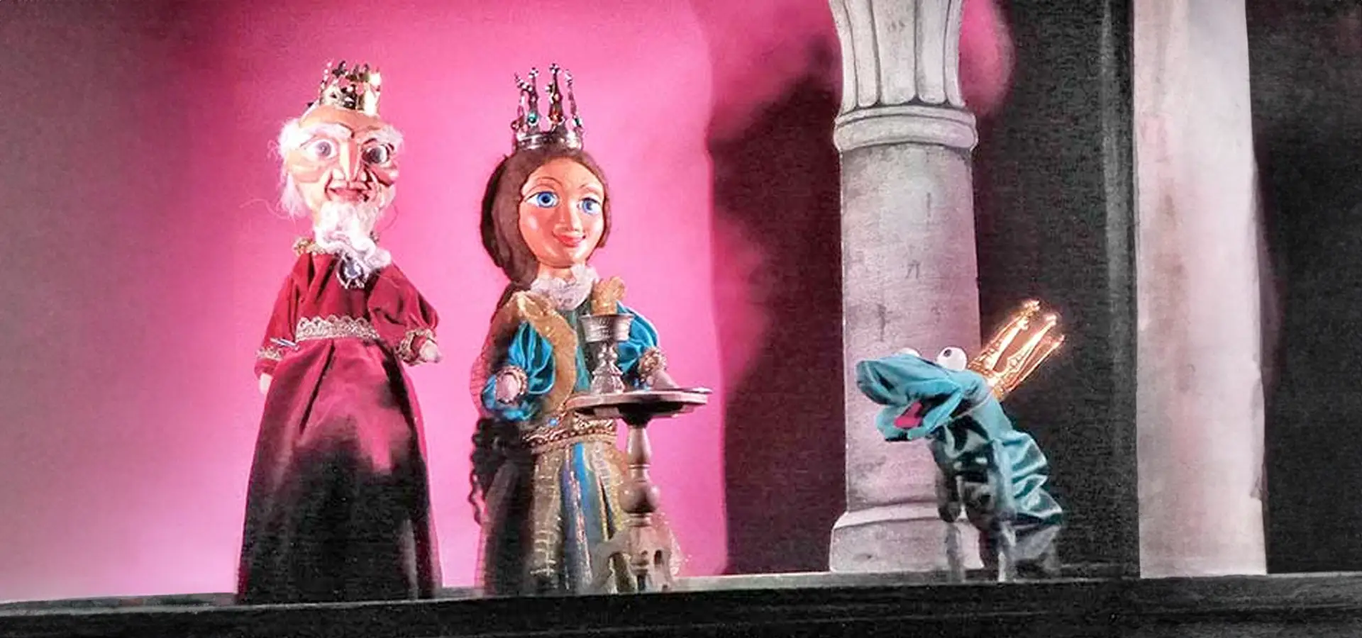 Marionettenkönig, -königin und Froschkönig auf einer Bühne.