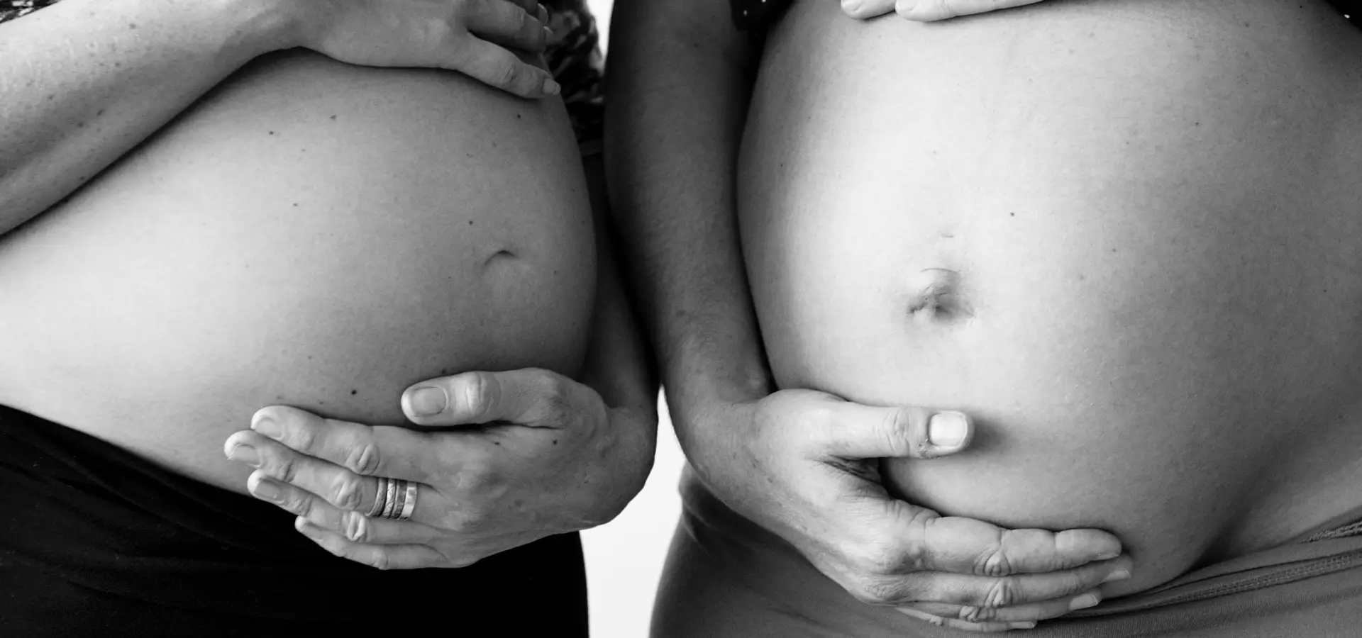 Zwei Personen halten ihre schwangeren Bäuche in Schwarz-Weiß.
