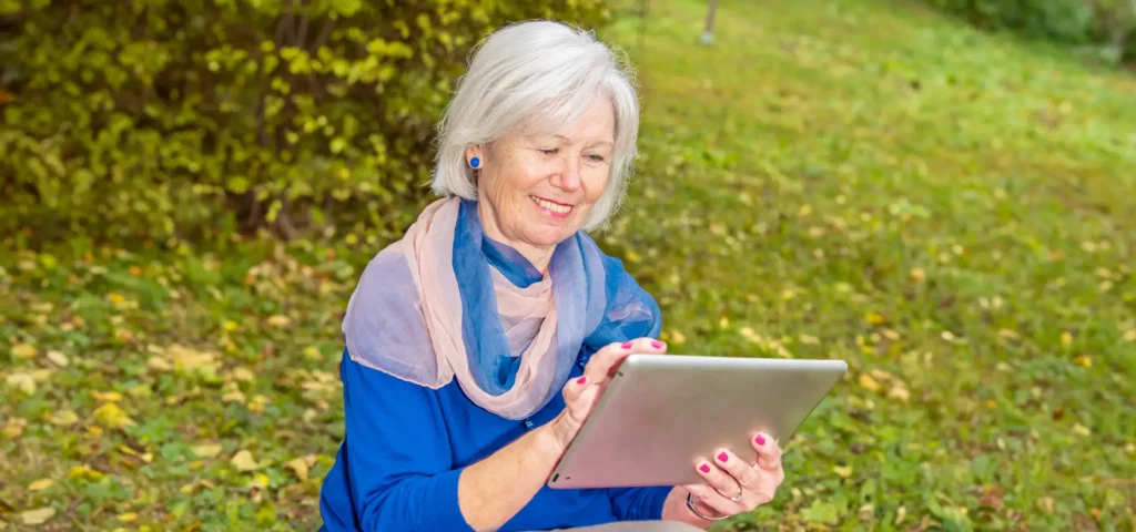 Ältere Dame lächelt beim Betrachten eines Tablets im Park.