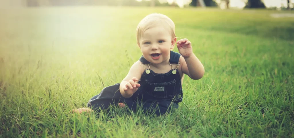 Lachendes Kleinkind im Gras sitzend.