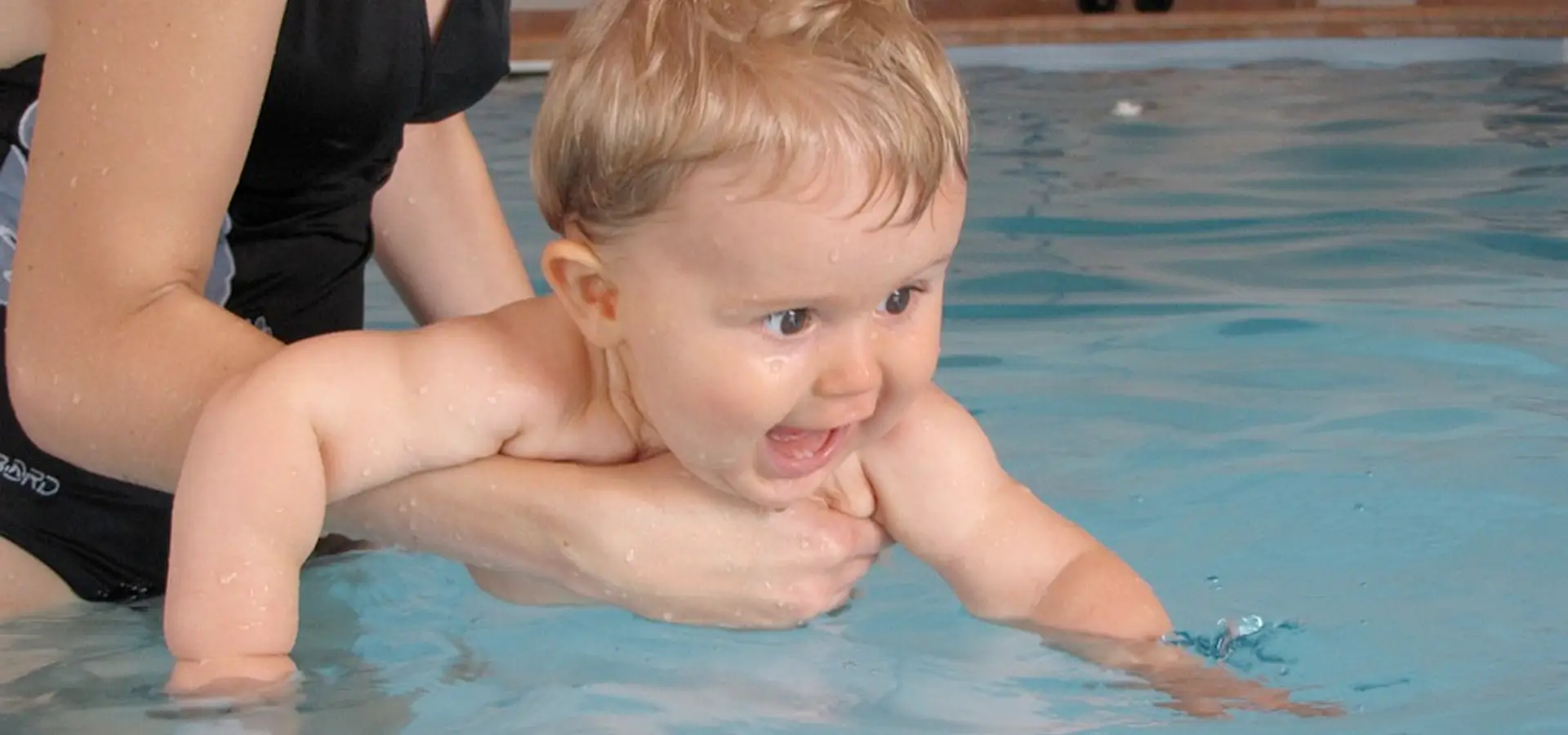 Kleinkind beim Babyschwimmen, strahlend im Wasser.