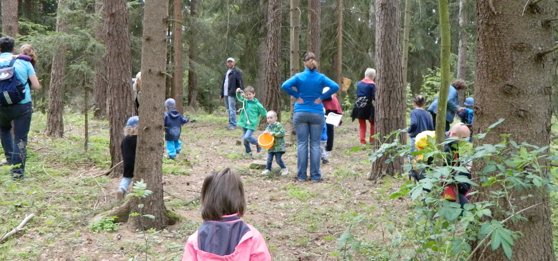Gruppe von Menschen und Kindern im Wald bei Outdoor-Aktivitäten.