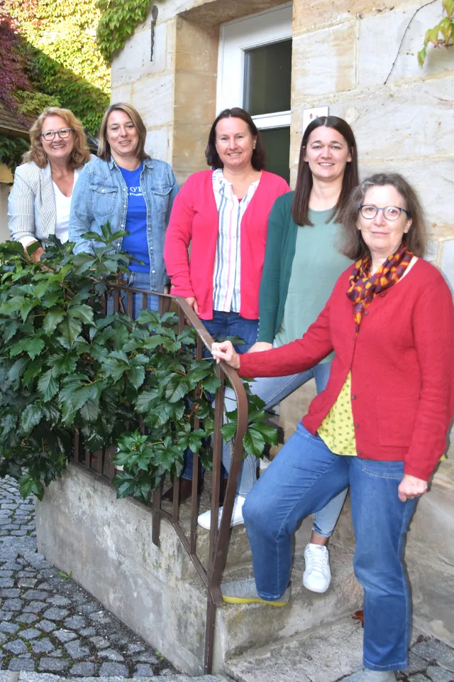 Fünf Frauen lächelnd auf einer Außentreppe stehend.