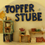 Keramikwerkstatt-Schild "Töpfer Stube" mit Miniatur-Töpferwaren.