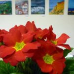 Rote Blumen im Vordergrund, Gemäldeausstellung im Hintergrund.