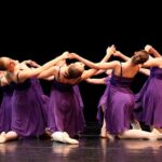 Tänzerinnen in purpurfarbenen Kleidern bei einer Ballettauﬀührung.