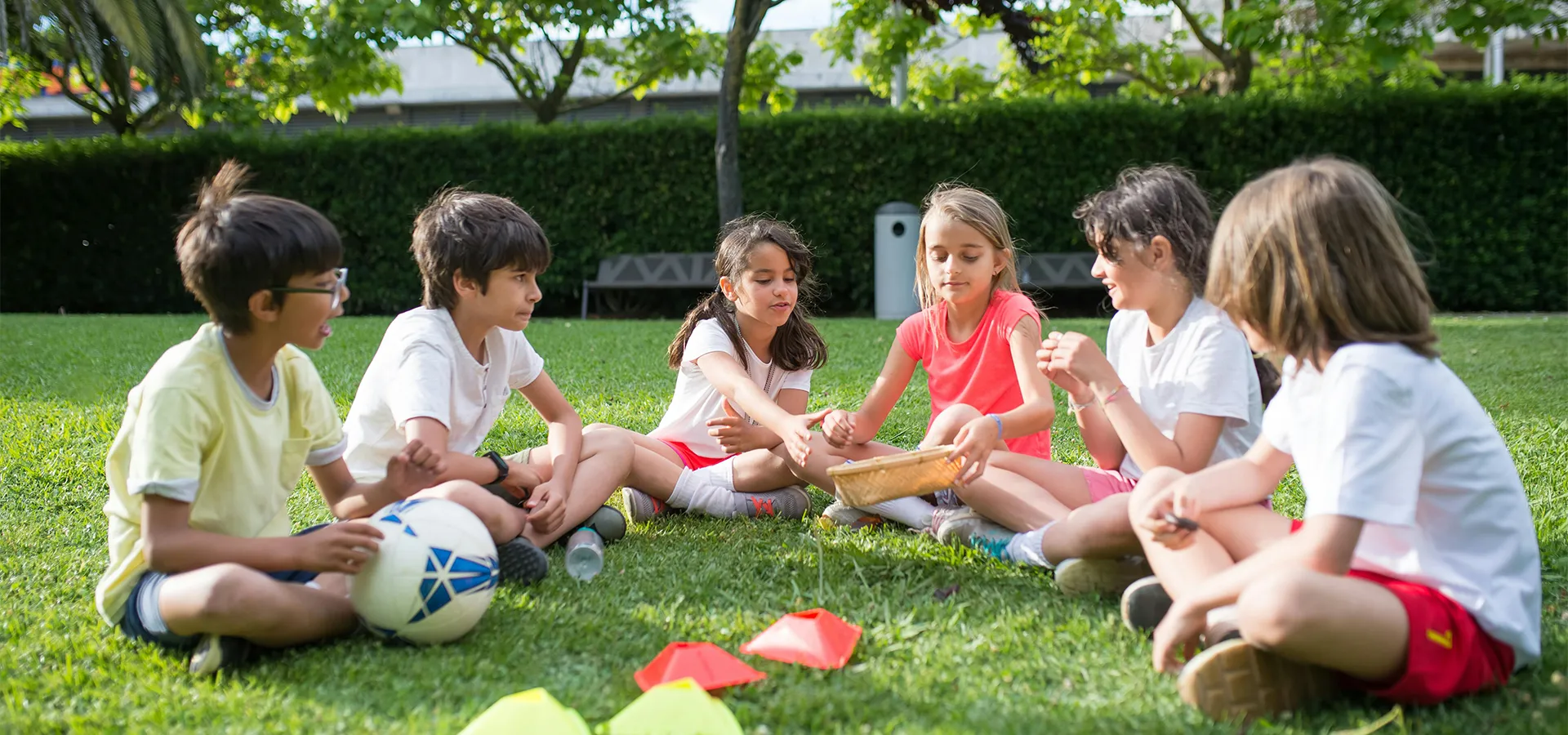 Kinder spielen zusammen im Gras mit einem Fußball und Konen.