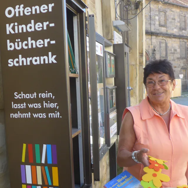 Erna Schmidth neben öﬀentlichem Bücherschrank auf der Straße.