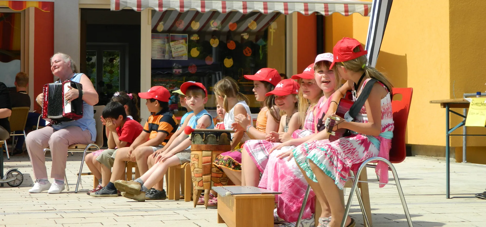 Gruppe von Kindern hört Akkordeonmusik bei sonnigem Wetter.