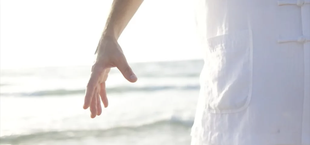 Hand einer Person im Sonnenlicht am Strand.