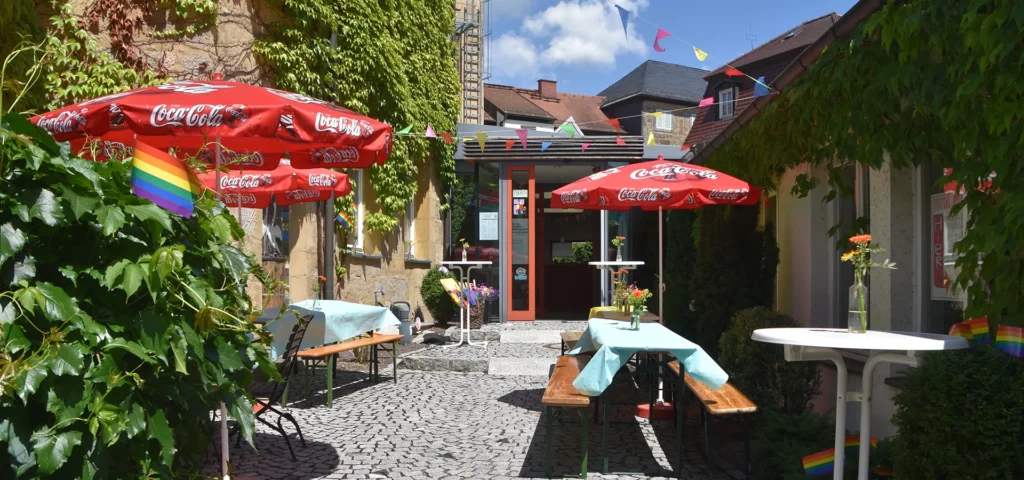 Gemütlicher Außenbereich eines Cafés mit Sonnenschirmen und Wimpelkette.