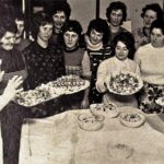 Gruppe von Frauen präsentiert hausgemachtes Essen bei einer Veranstaltung.