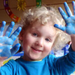 Kind zeigt stolz bemalte blaue Hände.