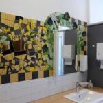 Wand mit buntem Mosaikspiegel und Waschbecken.