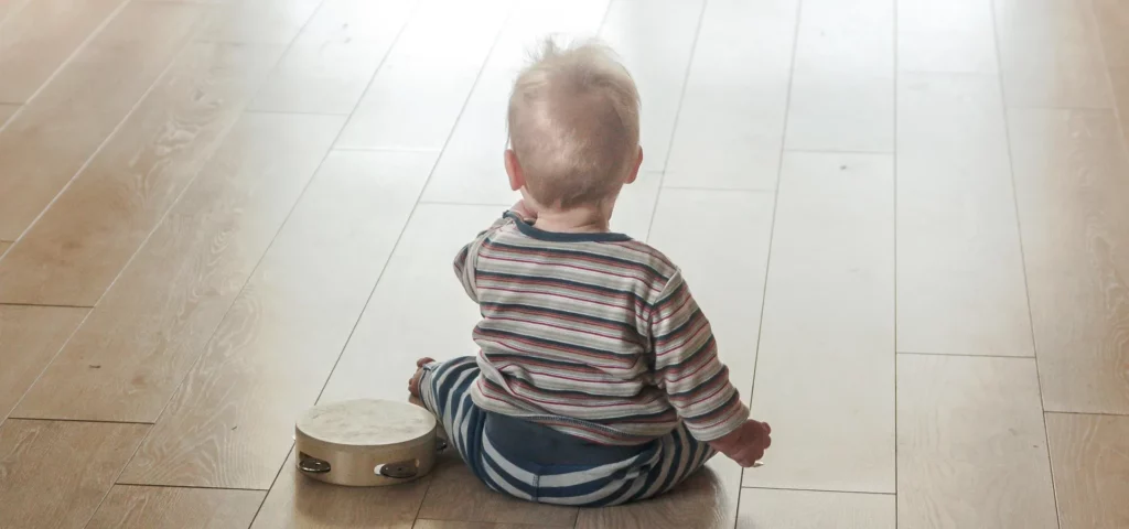 Baby von Hinten sitzt auf dem Boden mit Tambourin